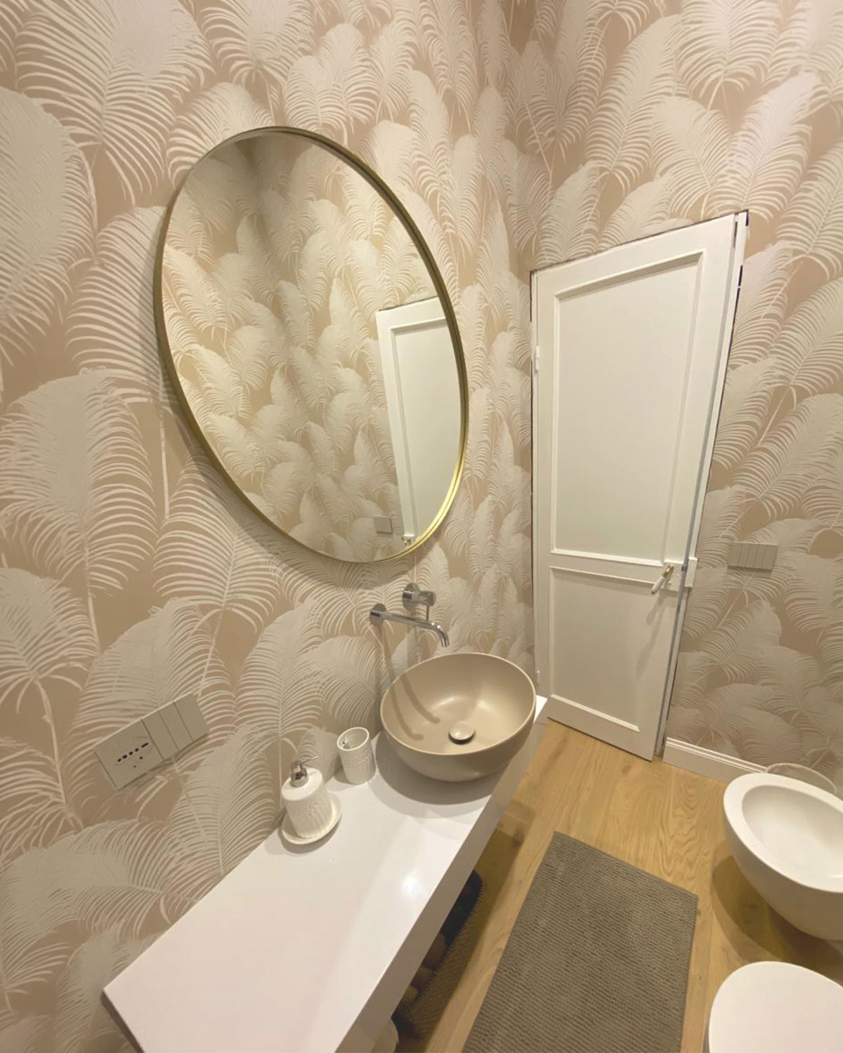 Bagno di servizio con carta da parati a foglie, specchio tondo in ottone e lavabo da appoggio
