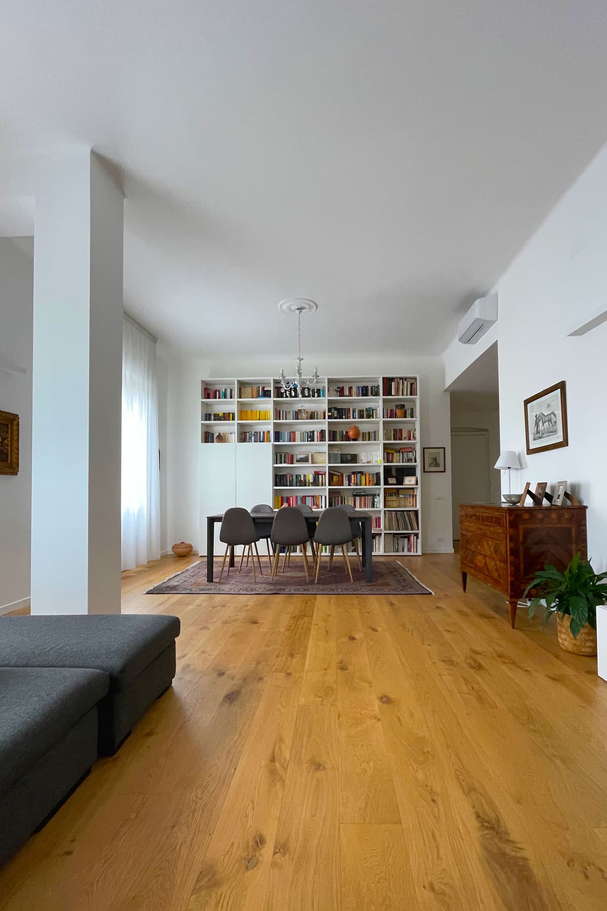 Zona pranzo con libreria bianca a tutta parete e parquet in rovere a plance larghe