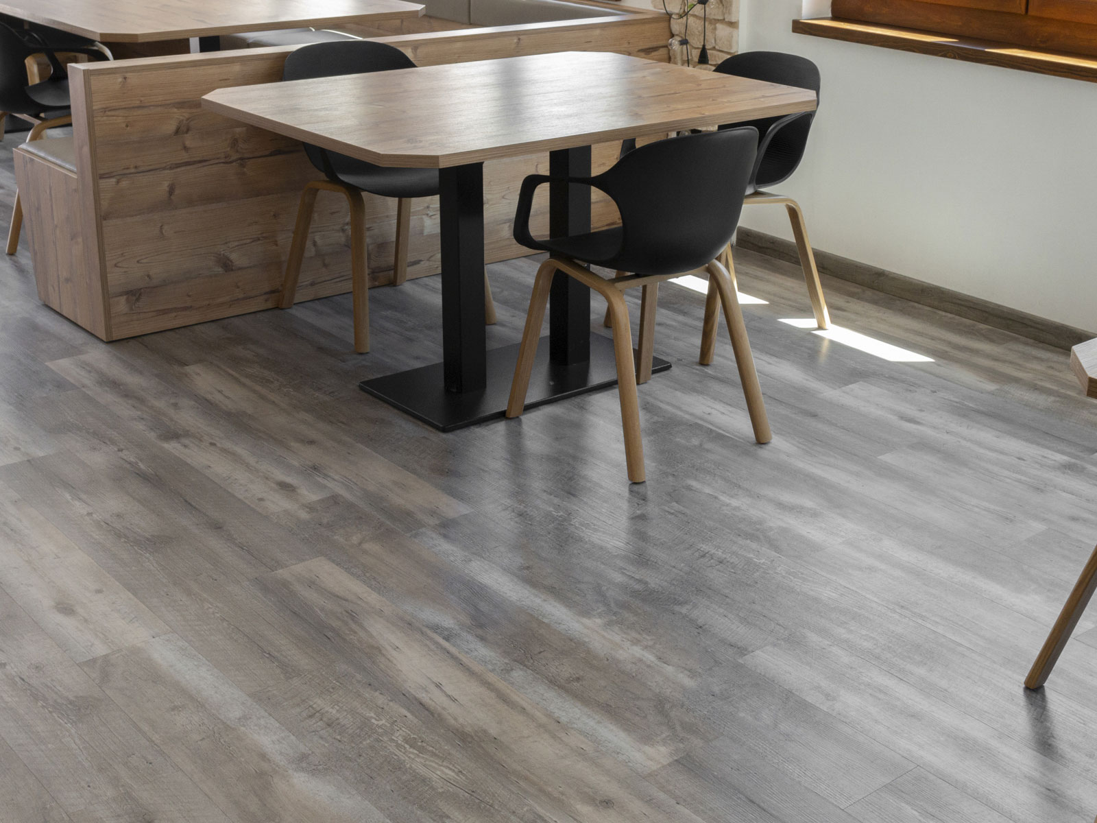 Pavimento SPC effetto legno grigio a doghe in una sala con tavoli in legno