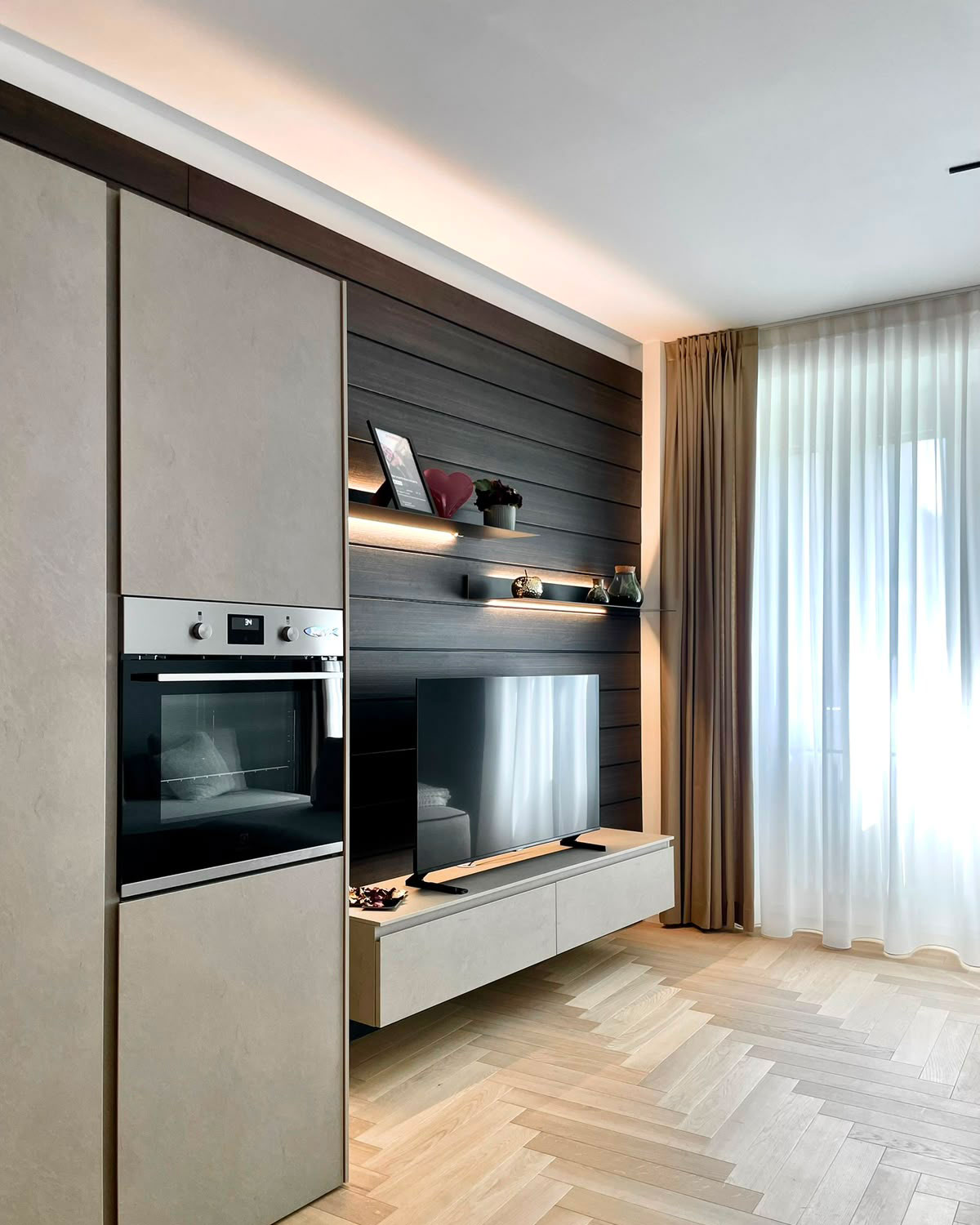Colonne forno in gres e parete attrezzata in legno scuro con mensole illuminate e mobile TV sospeso