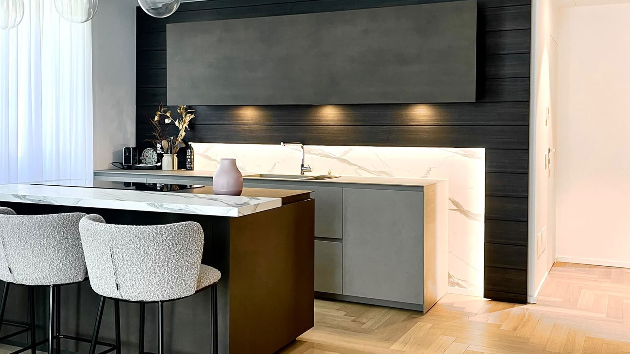 Cucina con isola in marmo, parete in legno scuro e parquet a spina nell'appartamento a Milano