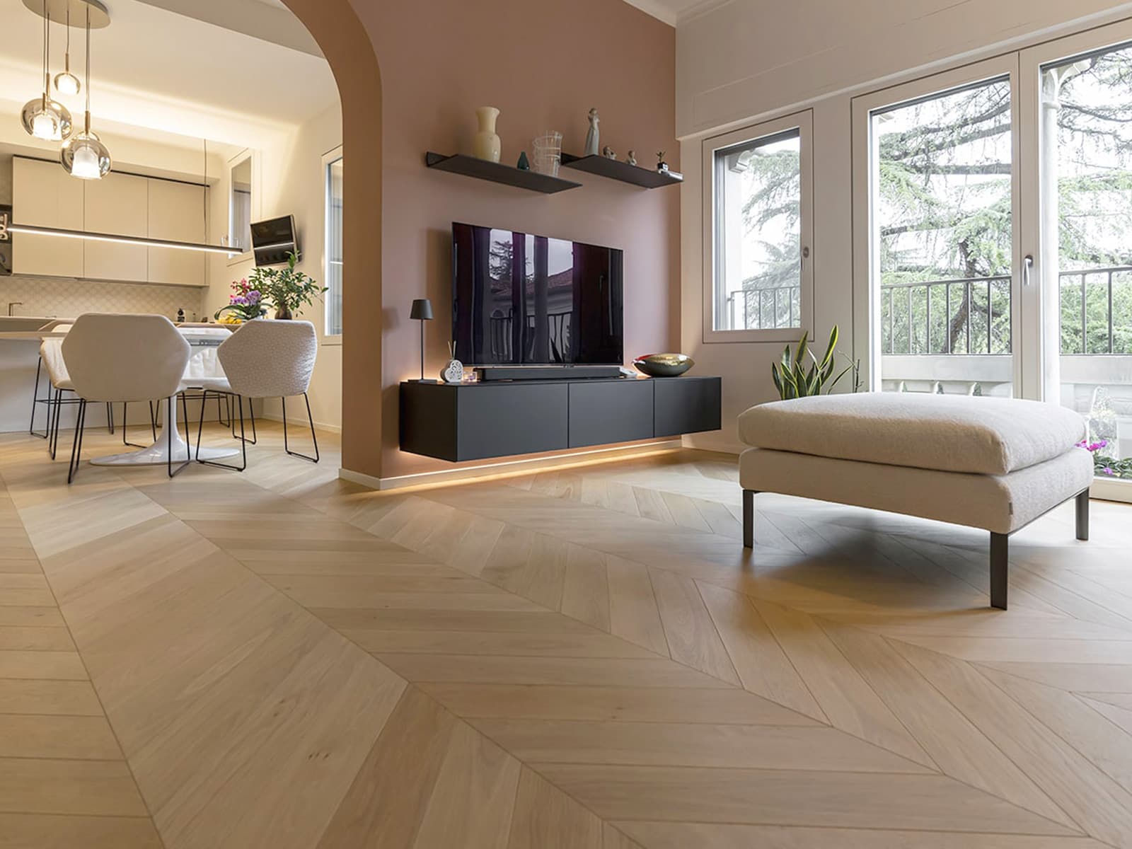 Living con parquet in rovere chiaro posato a spina francese, parete rosa antico e zona pranzo
