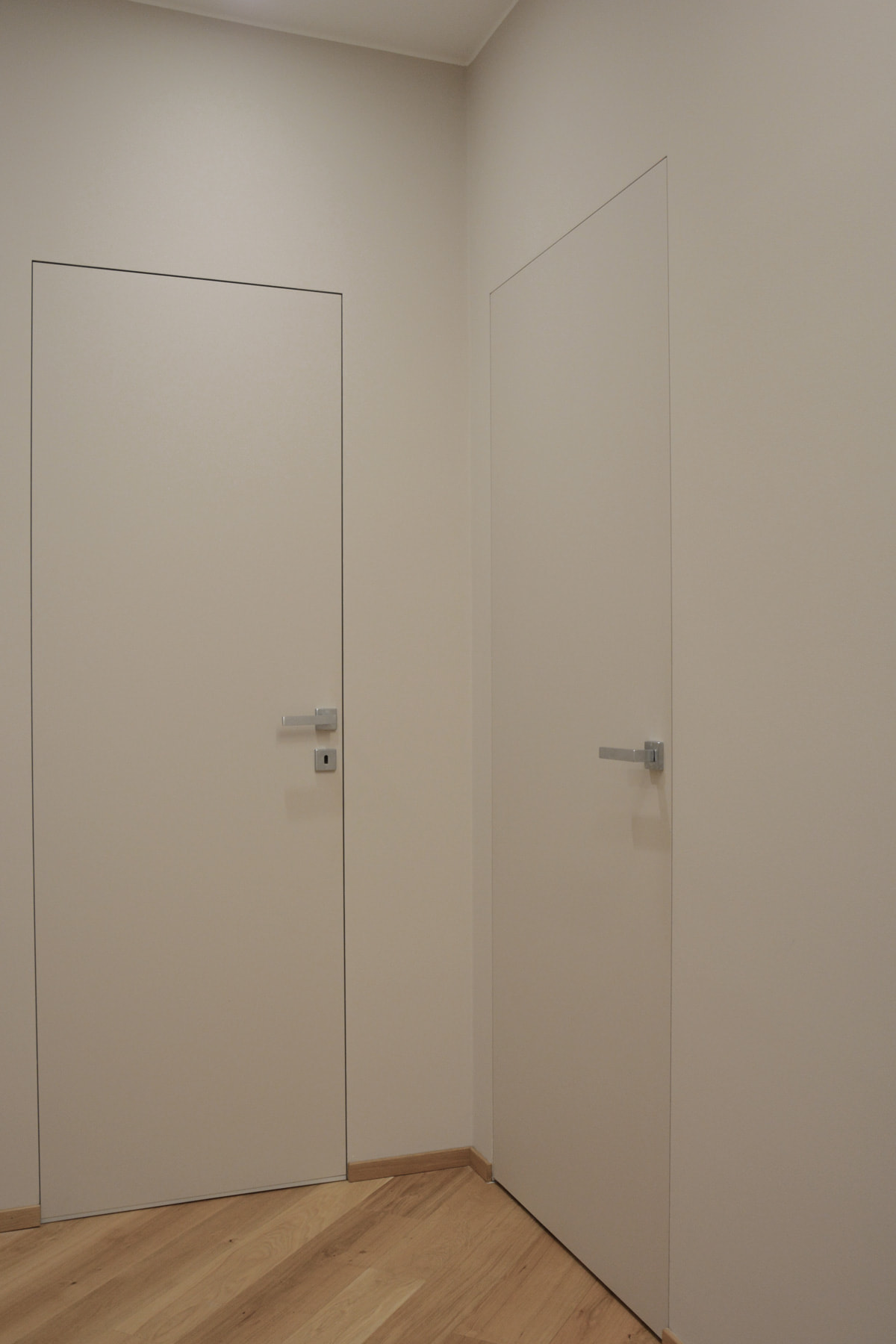 Porte rasomuro a tutta altezza tinta parete con maniglie cromate e parquet in rovere