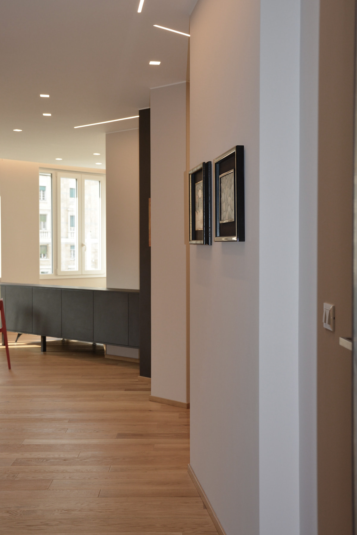 Corridoio con tagli di luce a soffitto che si apre sul living con madia grigia e parquet in rovere