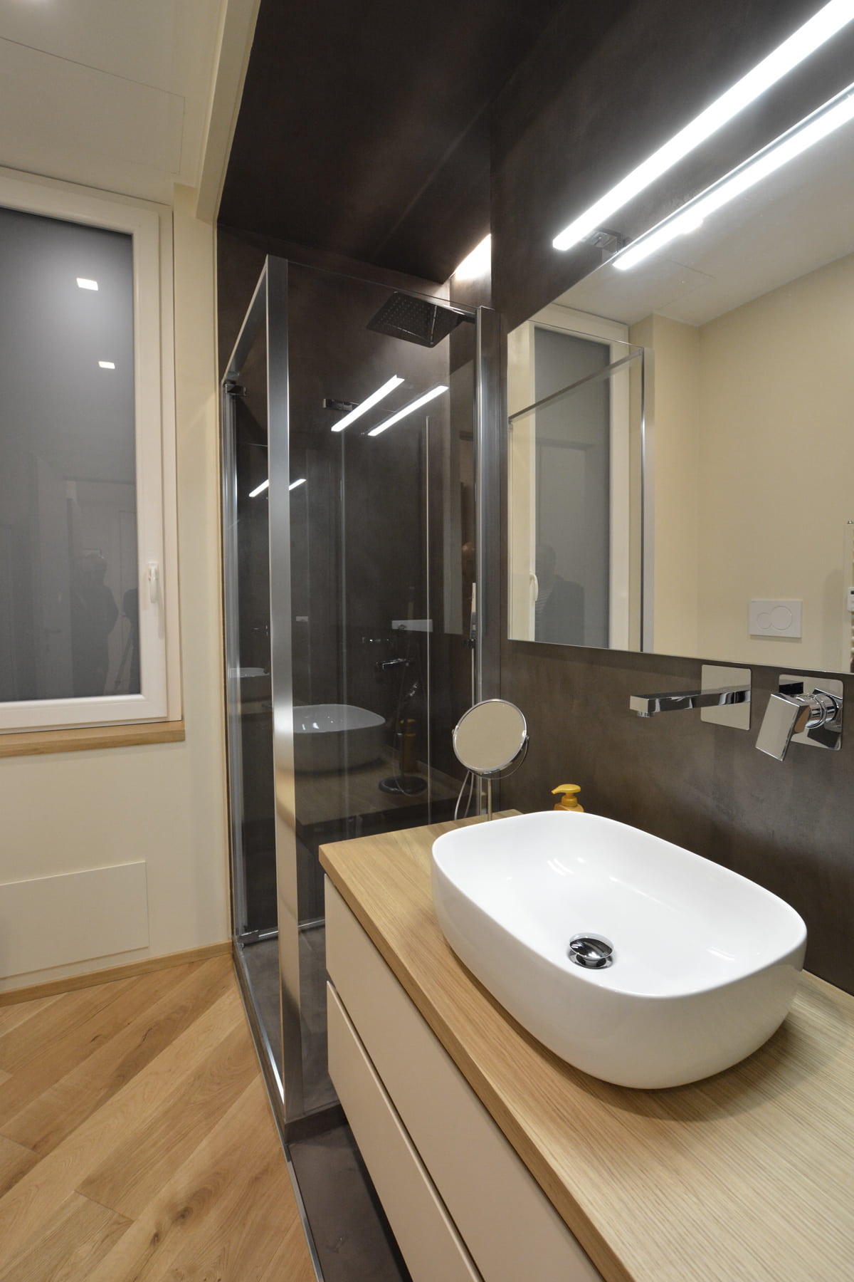Bagno con box doccia in cristallo, rivestimento in resina scura, mobile con top in rovere e lavabo da appoggio
