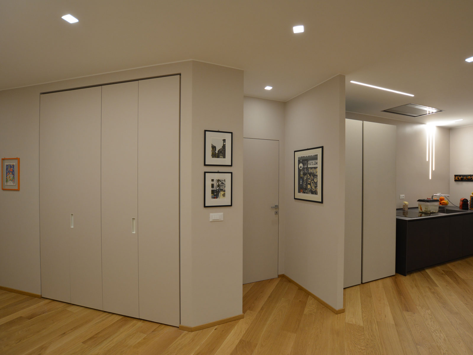 Ingresso con armadio a muro tinta parete, porta rasomuro e cucina scura sullo sfondo, parquet in rovere